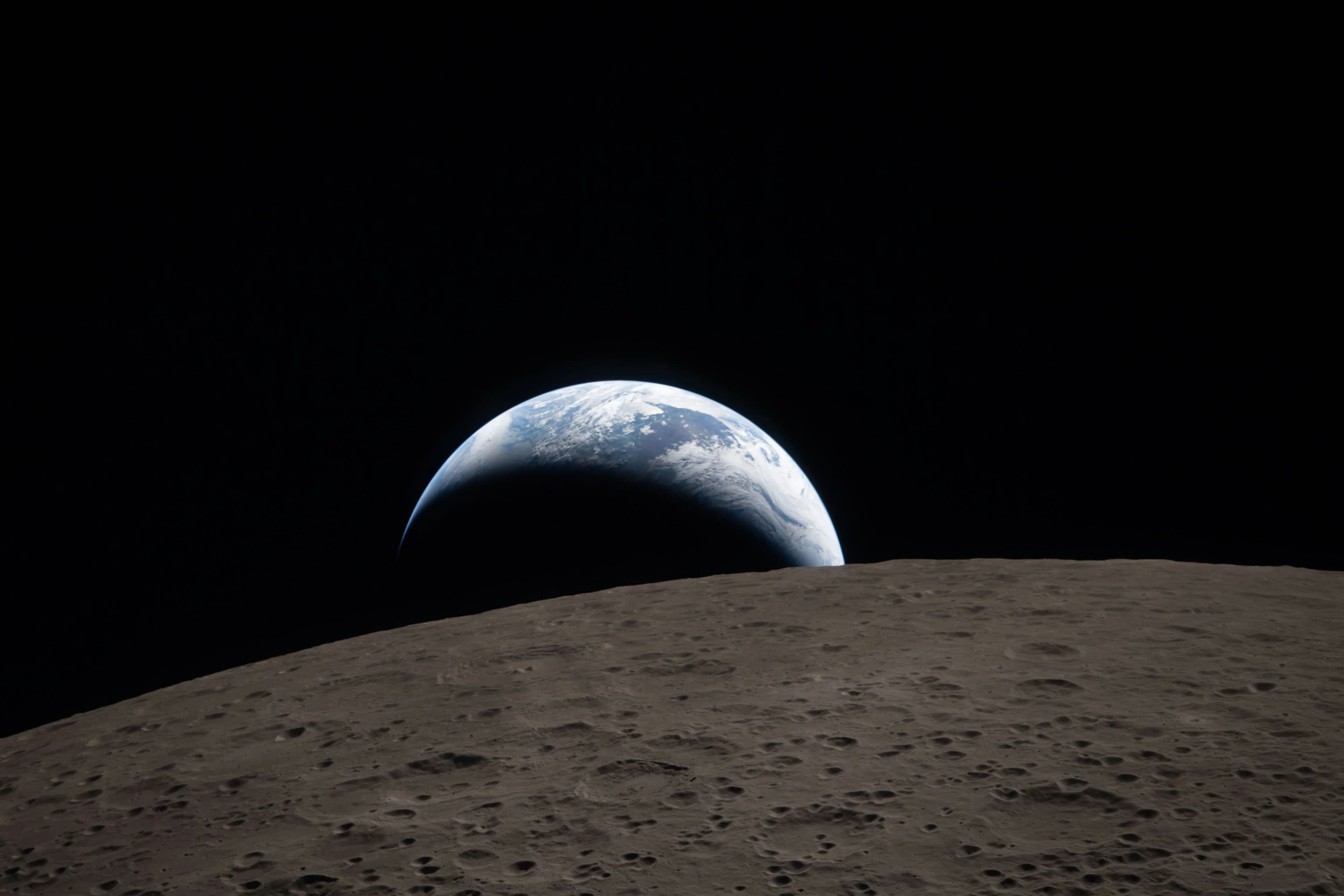 Earth, partly illuminated, rising low over the lunar horizon, photographed from Artemis II during the April 6 2026 lunar flyby. A modern echo of the 1968 Apollo 8 Earthrise.